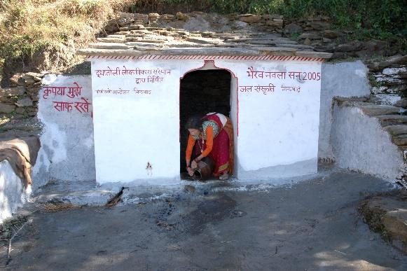 A covered spring shelter with Hindi text painted on its walls