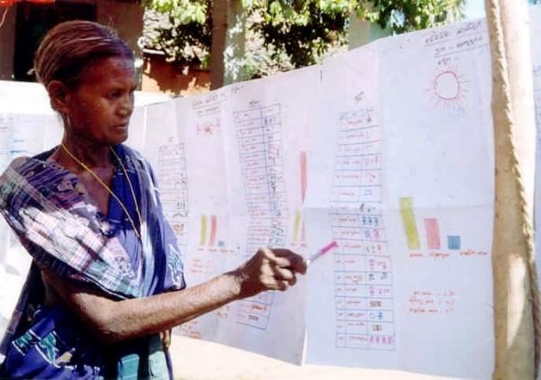 A woman points to a large hand drawn chart during a village meeting