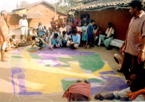 Villagers gather around a large coloured map drawn on the ground