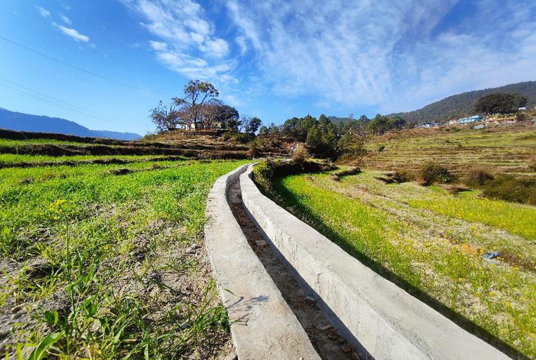 A lined irrigation channel runs between green terraces