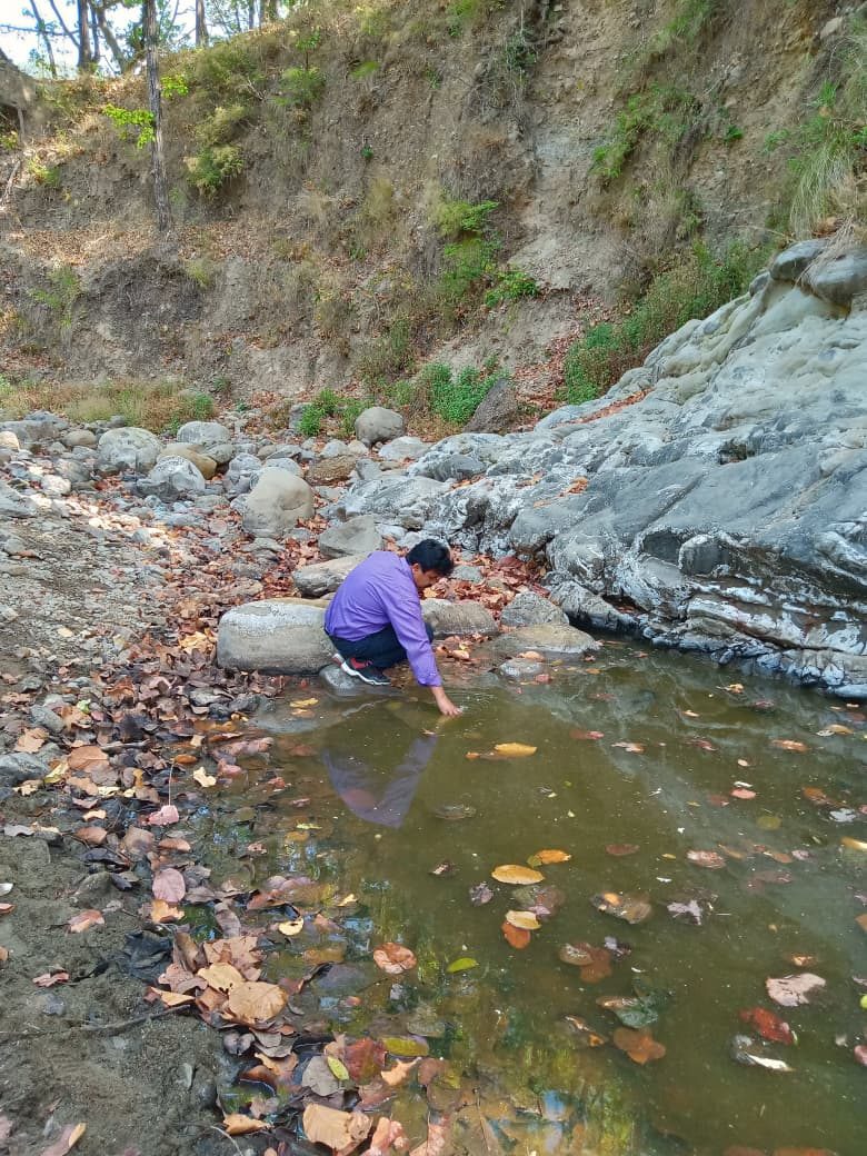 A man collects water from a rocky stream bed