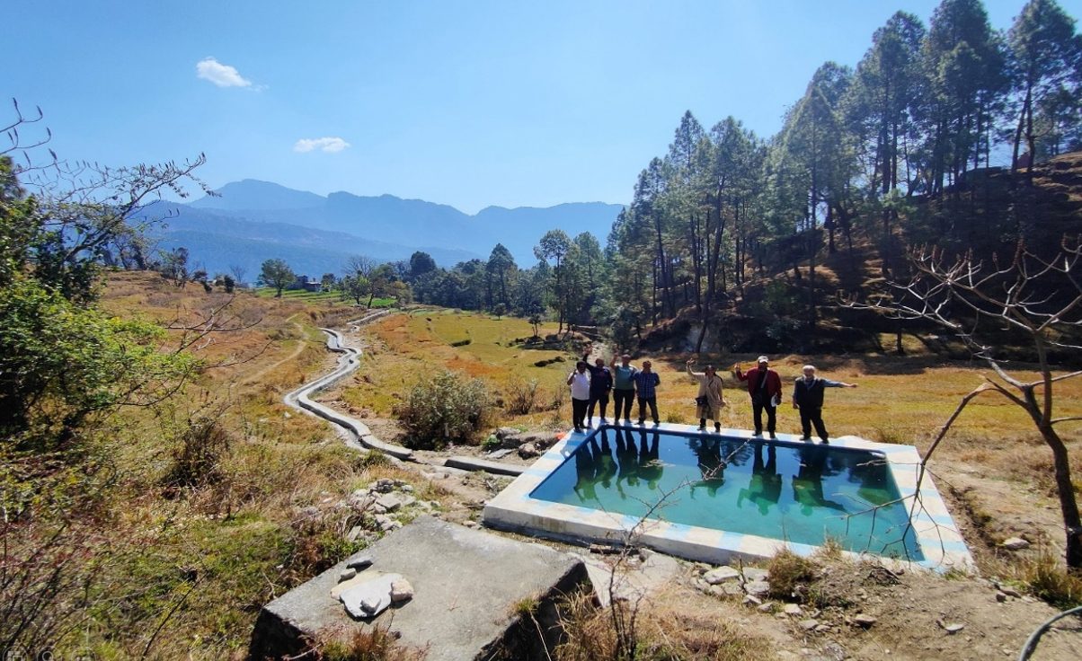 A blue water tank in a dry valley with pine covered hills behind